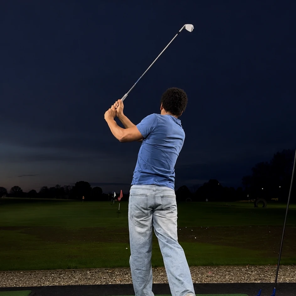 Crypto Seth mid swing at a floodlit driving range